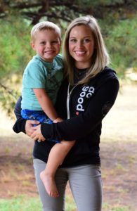 A woman wearing CURA's 'do good' hoodie, and holding her son.