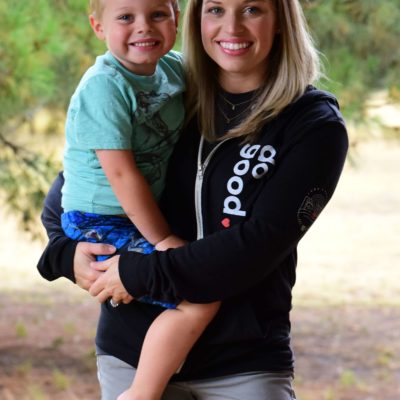 A woman wearing CURA's 'do good' hoodie, and holding her son.